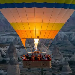 Hot air balloon over Cappadocia at sunrise with passengers and burner flame