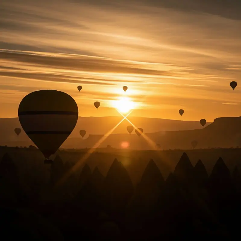 Siluetas de numerosos globos aerostáticos elevándose sobre las chimeneas de hadas de Capadocia al amanecer